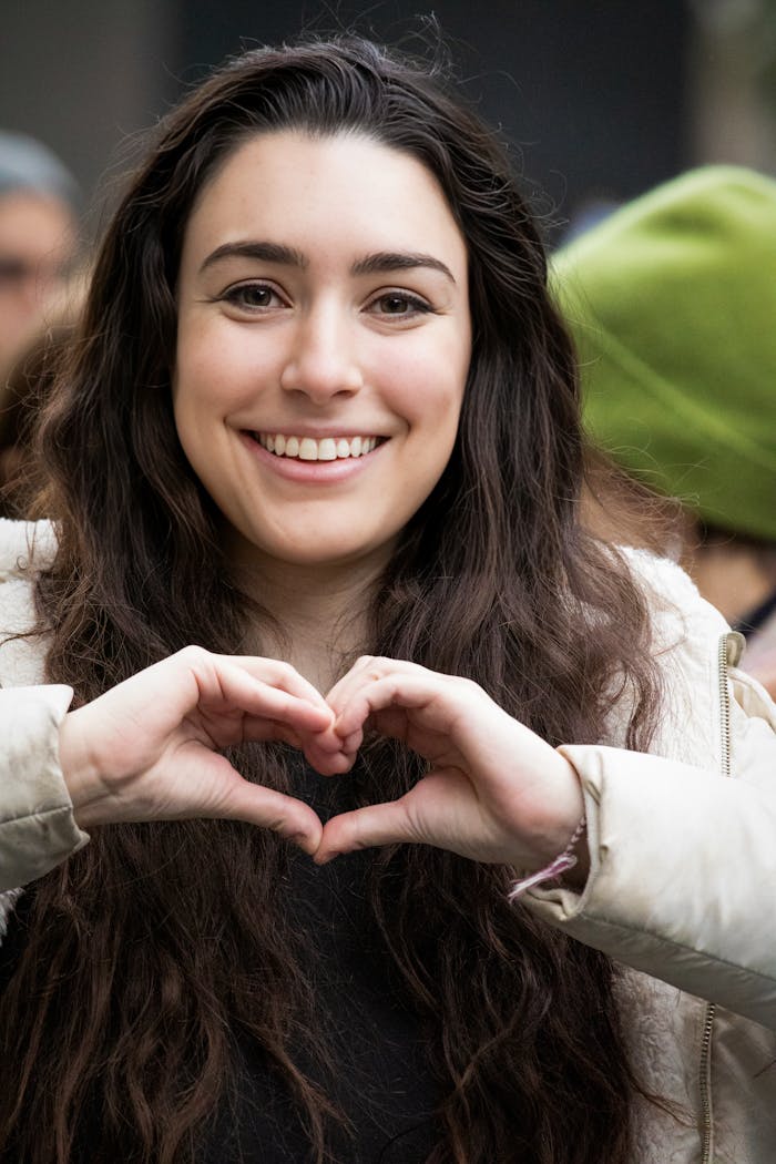 about-hero A happy woman in a urban setting making a heart shape with her hands, symbolizing love and positivity.